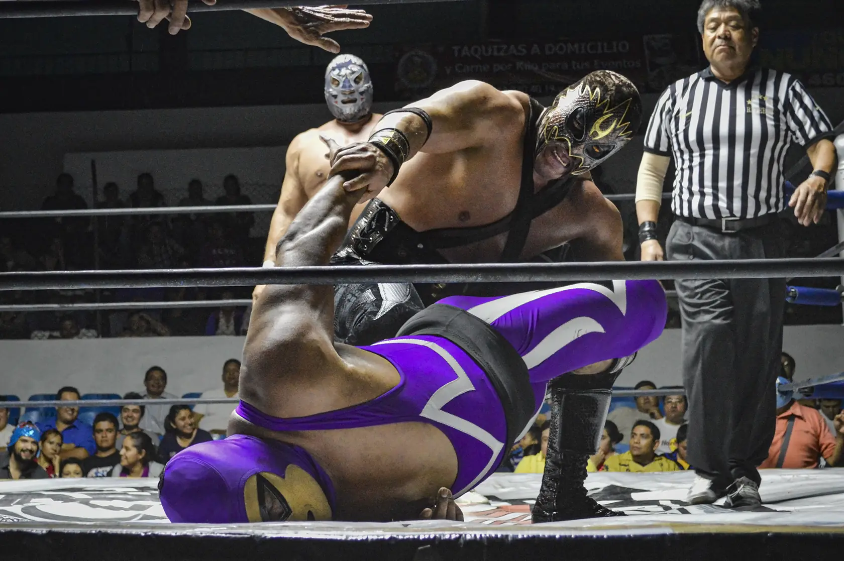 Two masked Lucha Libre wrestlers grappling in the ring during a live match